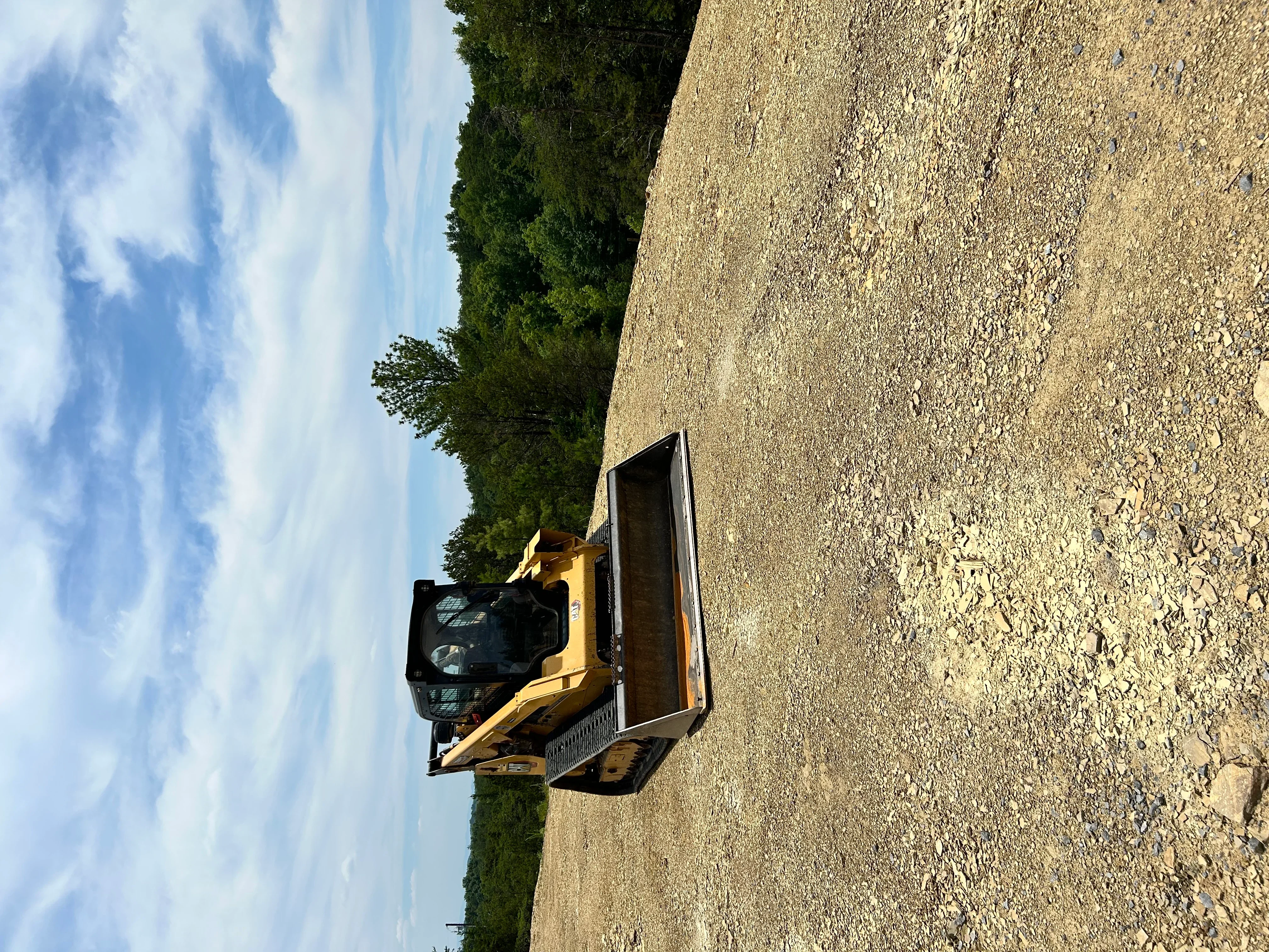 Compact track loader spreading and grading gravel driveway material on sloped residential site