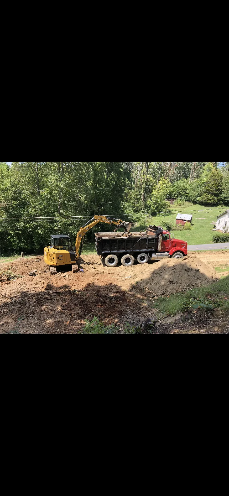 Compact excavator loading soil into dump truck during residential lot excavation