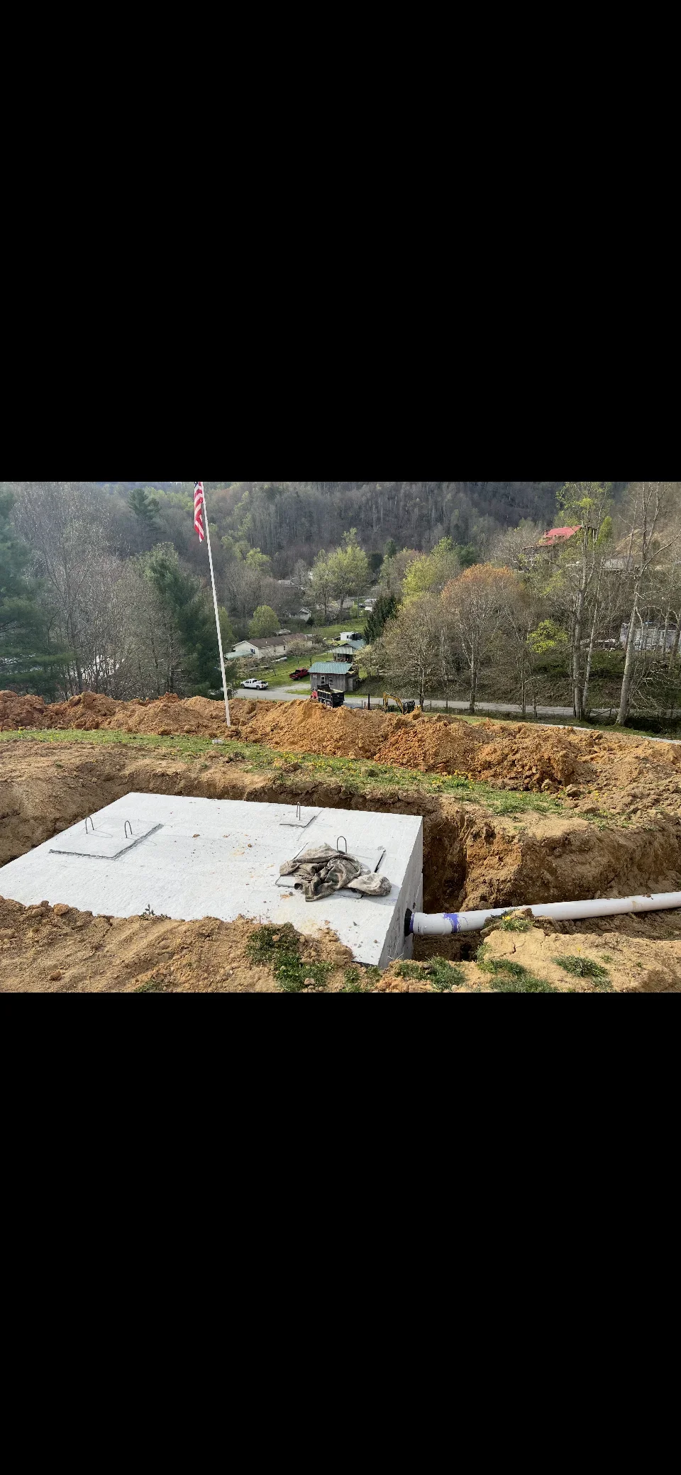 Concrete septic tank installed in excavated basin with PVC drainage pipe and rebar reinforcement