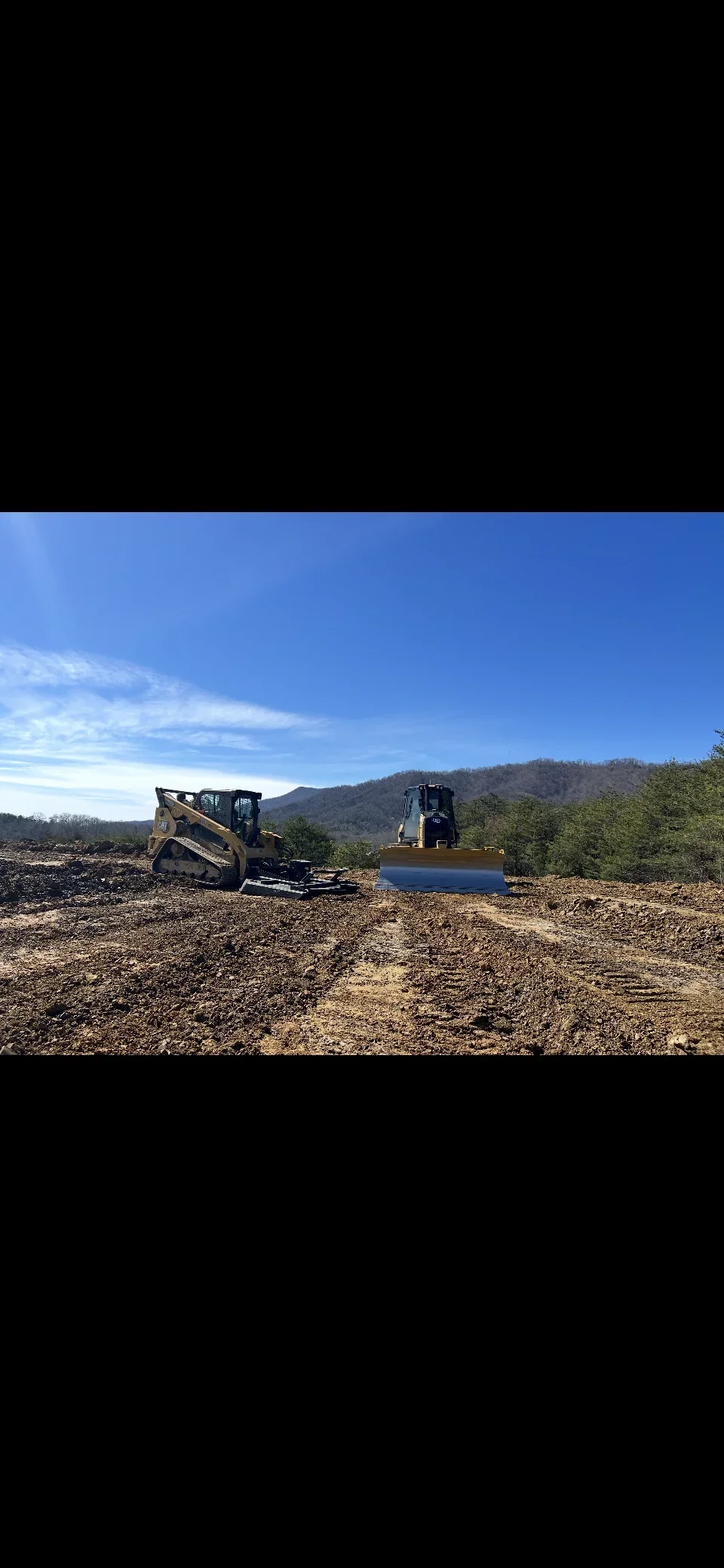 Skid steer loader and grader clearing and grading raw land with rocky debris