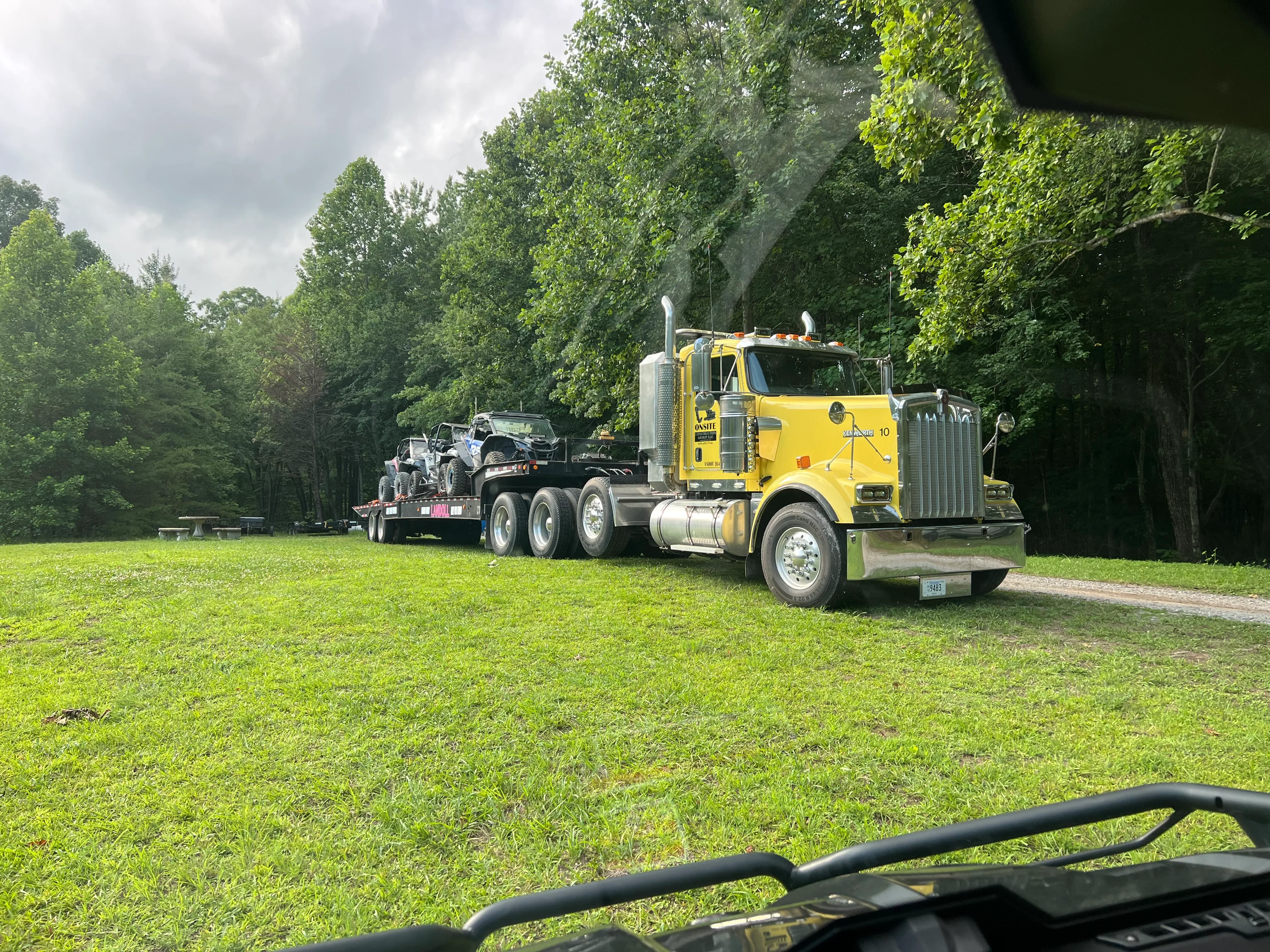 Yellow tractor-trailer with flatbed hauling heavy construction equipment on grass field