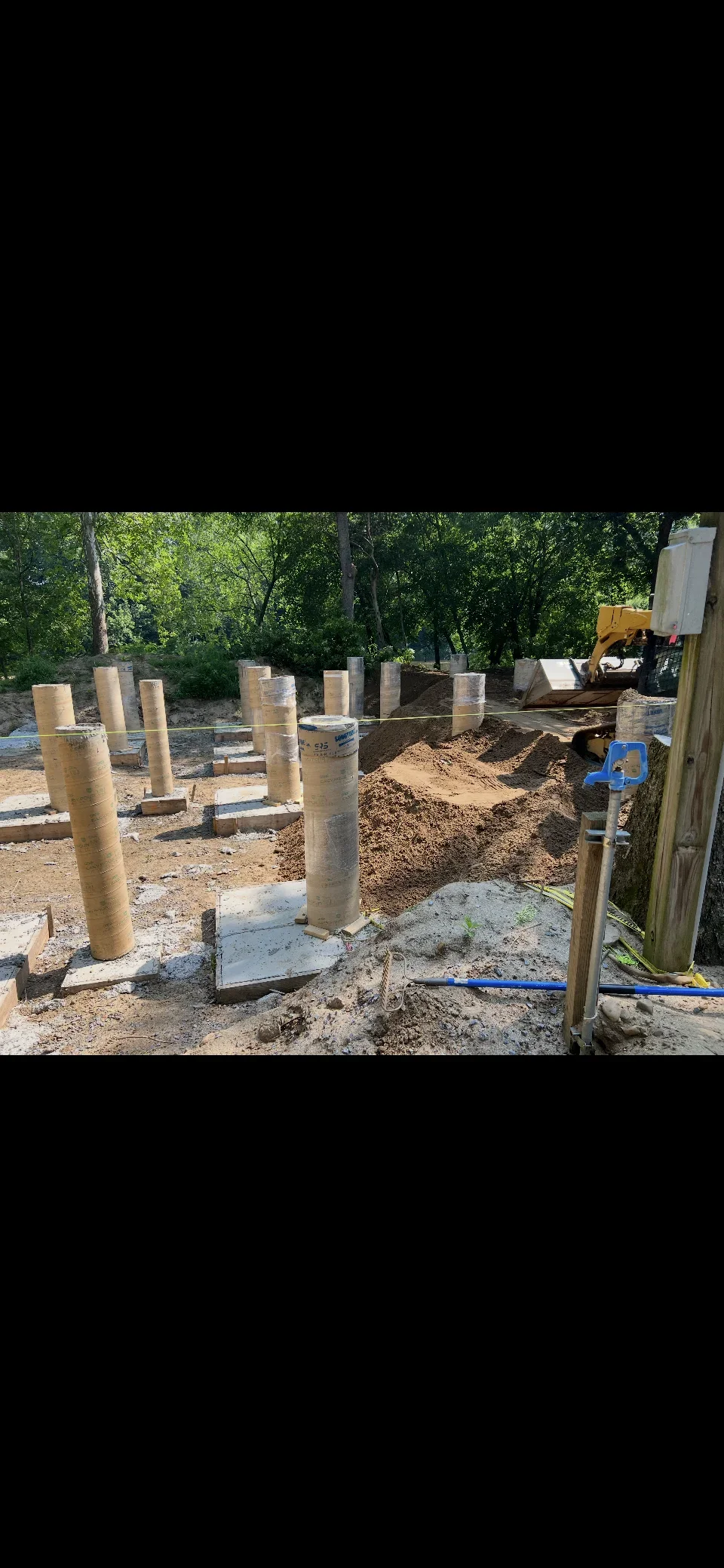 Concrete pier foundations with footings, excavated soil, and gravel base preparation on construction site